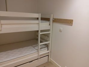Kerrossänky, jossa on puinen pääty ja valkoinen seinä.