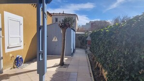 A narrow paved pathway flanked by buildings with a small tree and a hedge. - Renovated villa with AC, pool & parking near the sea (Cap d'Agde)