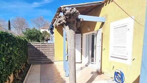 A yellow building with a wooden staircase leading to a door, a tree in the center, and a blue hose on the ground. - Renovated villa with AC, pool & parking near the sea (Cap d'Agde)