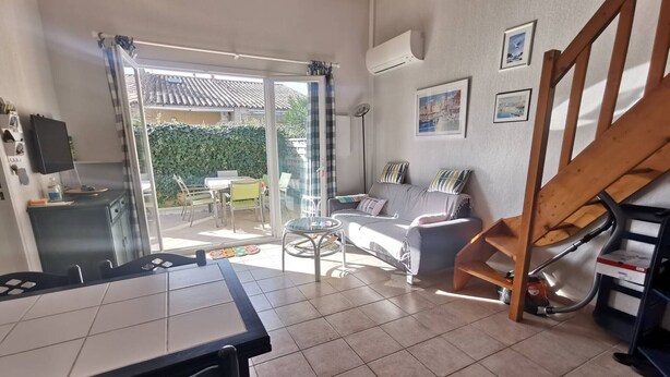 A living room with a sofa, a dining table, and a kitchen area. - Renovated villa with AC, pool & parking near the sea (Cap d'Agde)