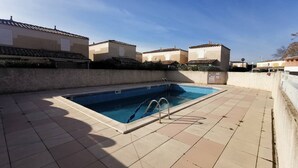 A swimming pool with a tiled deck, surrounded by buildings with similar architecture. - Renovated villa with AC, pool & parking near the sea (Cap d'Agde)