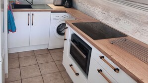 A compact kitchen with a washing machine, oven, and a wooden countertop. - Renovated villa with AC, pool & parking near the sea (Cap d'Agde)