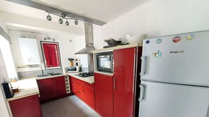 Une cuisine de taille réduite avec des meubles rouges, un réfrigérateur blanc et un four à micro-ondes.
