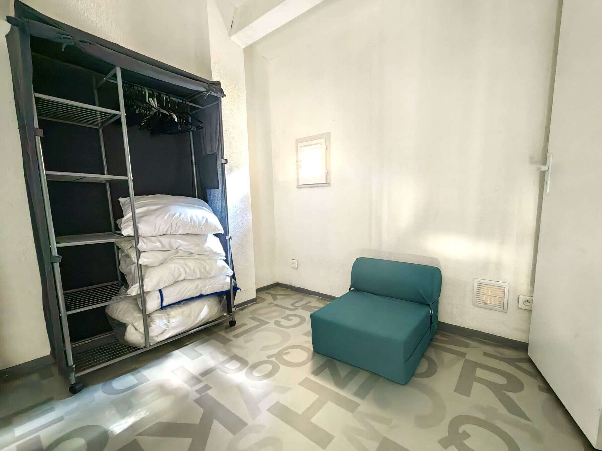 Een kamer met een metalen schap waarop kussens liggen en een smaragdgroene, beklede bank.