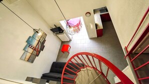 Un intérieur moderne avec un escalier en colimaçon rouge, un canapé noir et un coin repas avec des chaises rouges.