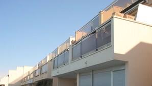 Een meerhoog gebouw met balkons, grote ramen en een witte omheining.
