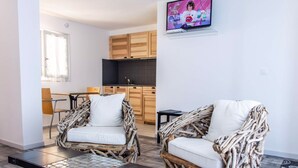 Een moderne woonkamer met rieten meubels, een flatscreen televisie en een keuken op de achtergrond.