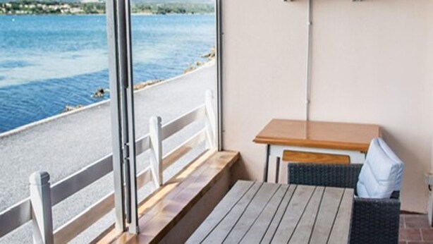Een balkon met een tafel en stoelen, met uitzicht op een waterpartij en een verre kustlijn.