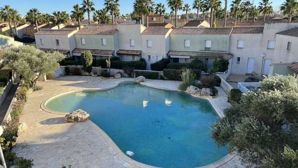 A swimming pool with a curved edge, surrounded by stone tiles and greenery. - Stylish 2BR Apt with Pool, AC & Terrace - Sleeps 6, 600m from Beach (Valras-Plage)