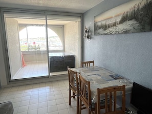 A dining area with a table and chairs, a sliding glass door leading to a balcony, and a painting on the wall. - Air-Conditioned T2 Near Beach with Pool and Parking (Cap d'Agde)