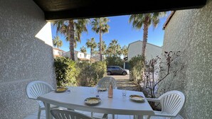A covered patio with a white table set for two, surrounded by white plastic chairs. - Cozy 3-Room Pavilion with Pool, Near Beach and Shops, Sleeps 6 (Valras-Plage)
