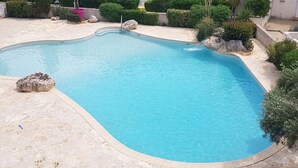 A swimming pool with a curved edge, surrounded by a stone deck and greenery. - Cozy 3-Room Pavilion with Pool, Near Beach and Shops, Sleeps 6 (Valras-Plage)
