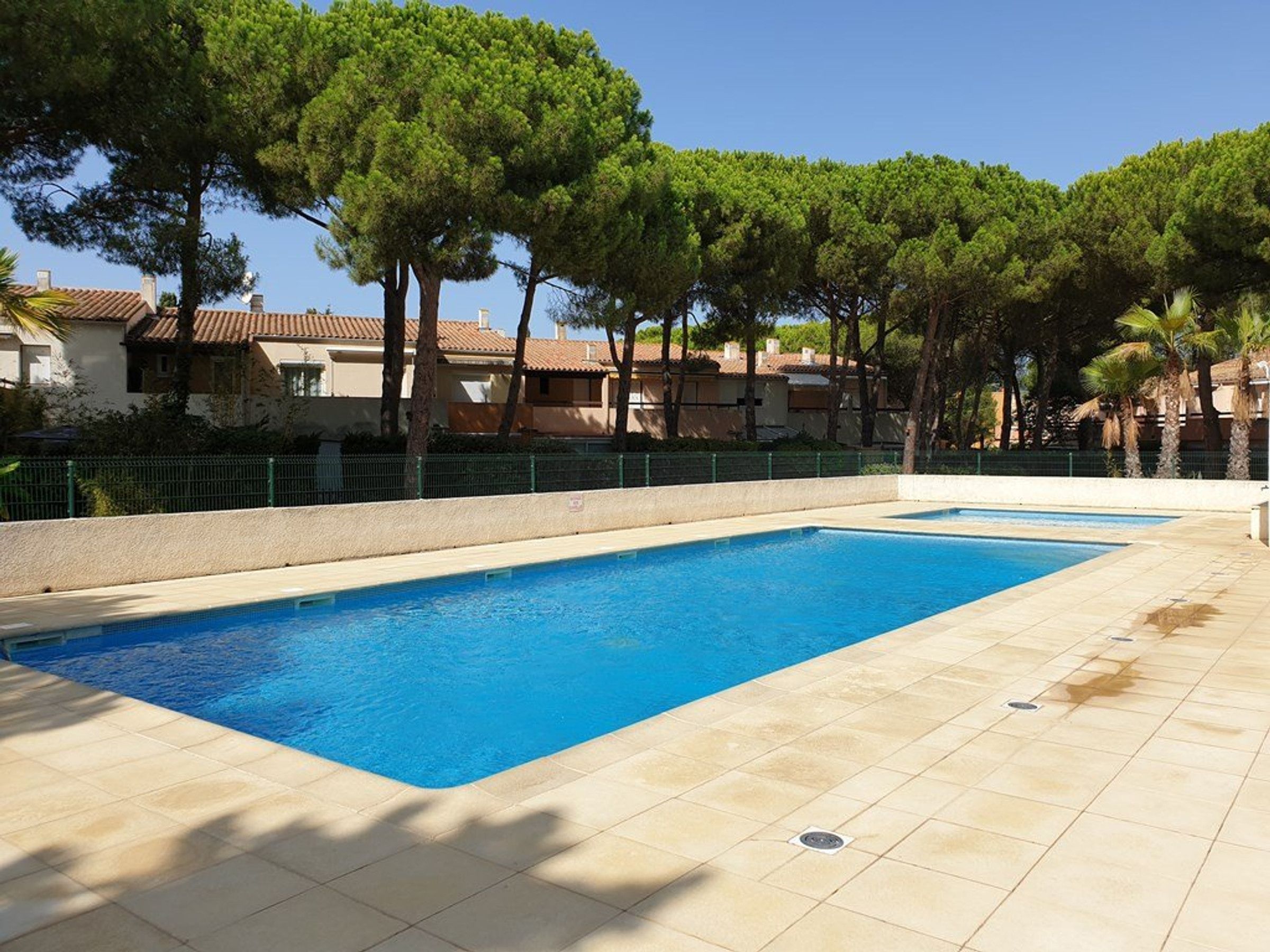 A swimming pool with a tiled deck, surrounded by trees and buildings.