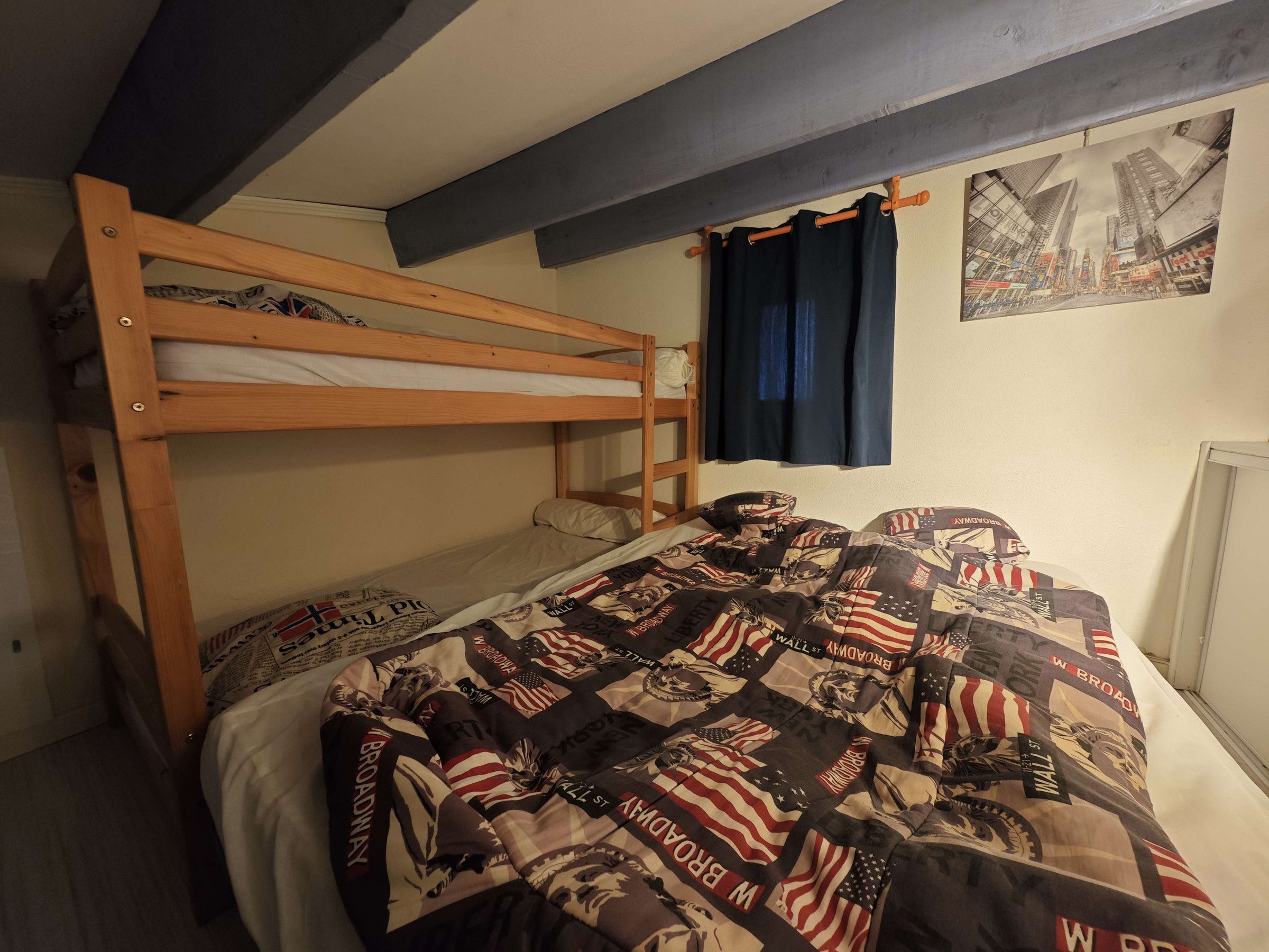 A bunk bed with a quilted blanket, a wooden headboard, and a wall-mounted curtain.