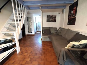 A living room with a staircase, a sofa, and a wall with a poster.
