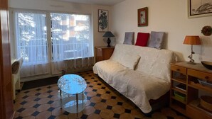 Un dormitorio con una cama, una mesita redonda pequeña, una mesita de noche y una ventana con cortinas.
