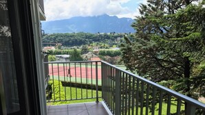 Un balcón con vistas a una cancha de tenis, árboles y montañas al fondo.