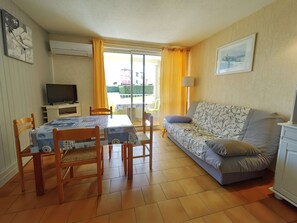 Uma sala de estar com sofá, uma mesa de jantar com cadeiras, televisão e varanda com cortinas amarelas.