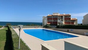 A swimming pool with a view of the sea, a building with a red roof, and a clear sky. - Charming A/C T2 with pool and parking, 20m from the sea, sleeps 5 (Cap d'Agde)