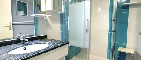 A modern bathroom with a glass-enclosed shower, a white sink, and a marble countertop.