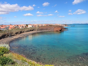 Uma área costeira com águas azul-claras, uma praia de areia e edifícios com telhados vermelhos.