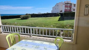 A balcony with a table and chairs, overlooking a grassy area and a building. - Charming A/C T2 with pool and parking, 20m from the sea, sleeps 5 (Cap d'Agde)