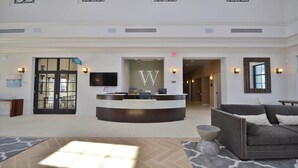 A hotel lobby with a reception desk, a large W-shaped wall decoration, a TV, and a couch. - Stunning 6BR Home • Pool, Spa, BBQ • Near Disney! (Kissimmee)