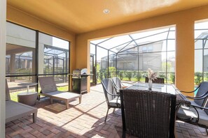 Eine Terrassenanlage im Freien mit Korbmöbeln, einem Grill und einer Glaskonstruktion.