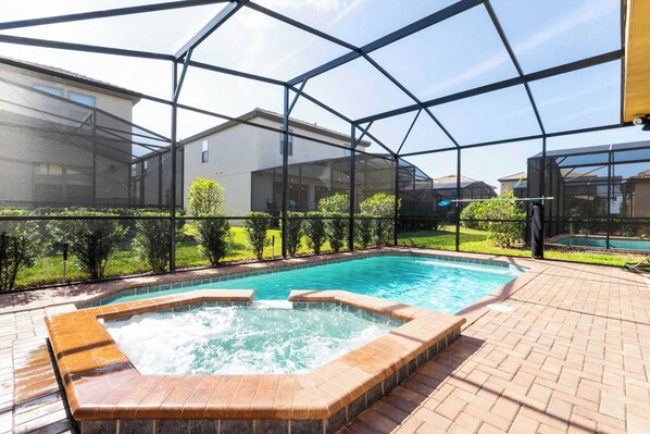 Ein Schwimmbad mit Whirlpool, umgeben von einer Glaskonstruktion und einer Ziegelterrasse.