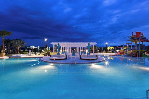 A swimming pool with a central seating area and a children's play structure.