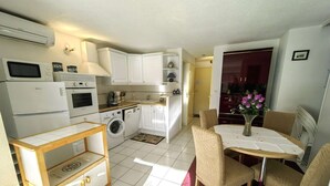 A compact kitchen with a microwave, oven, and washing machine. There is a dining area with a table and chairs.