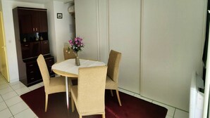 A dining area with a round table, beige chairs, a vase with flowers, and a dark red rug.