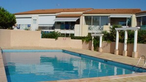 A swimming pool with tiled flooring, adjacent to a building with a tiled roof and a balcony.