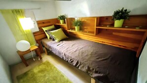 Un dormitorio pequeño y acogedor con una cama individual, una mesita de noche, una lámpara y una alfombra verde.