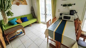 Una sala acogedora con un sofá verde, una mesa de comedor con sillas, un ventilador de techo y una planta en maceta.