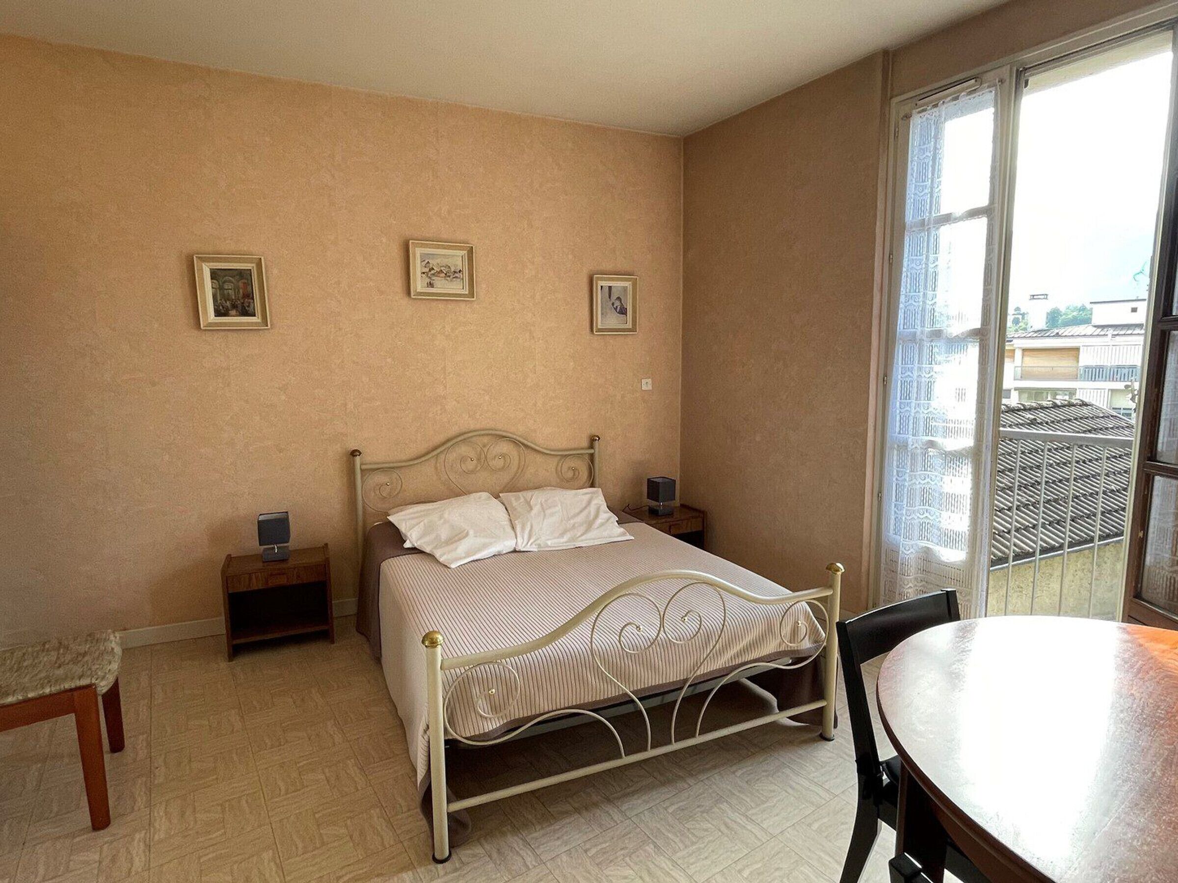 A bedroom with a bed, bedside tables, a chair, and a view of buildings through a window.