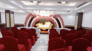 Ein Konferenzraum mit Reihen roter Stühle, die einer Bühne mit goldenem Hintergrund und floralen Dekorationen gegenüberliegen.
