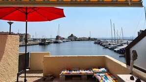A balcony with a view of a marina, a red umbrella, and colorful cushions. - T2 4 pers with pool, private parking, optional AC - Le Barcarès (Le Barcarès)