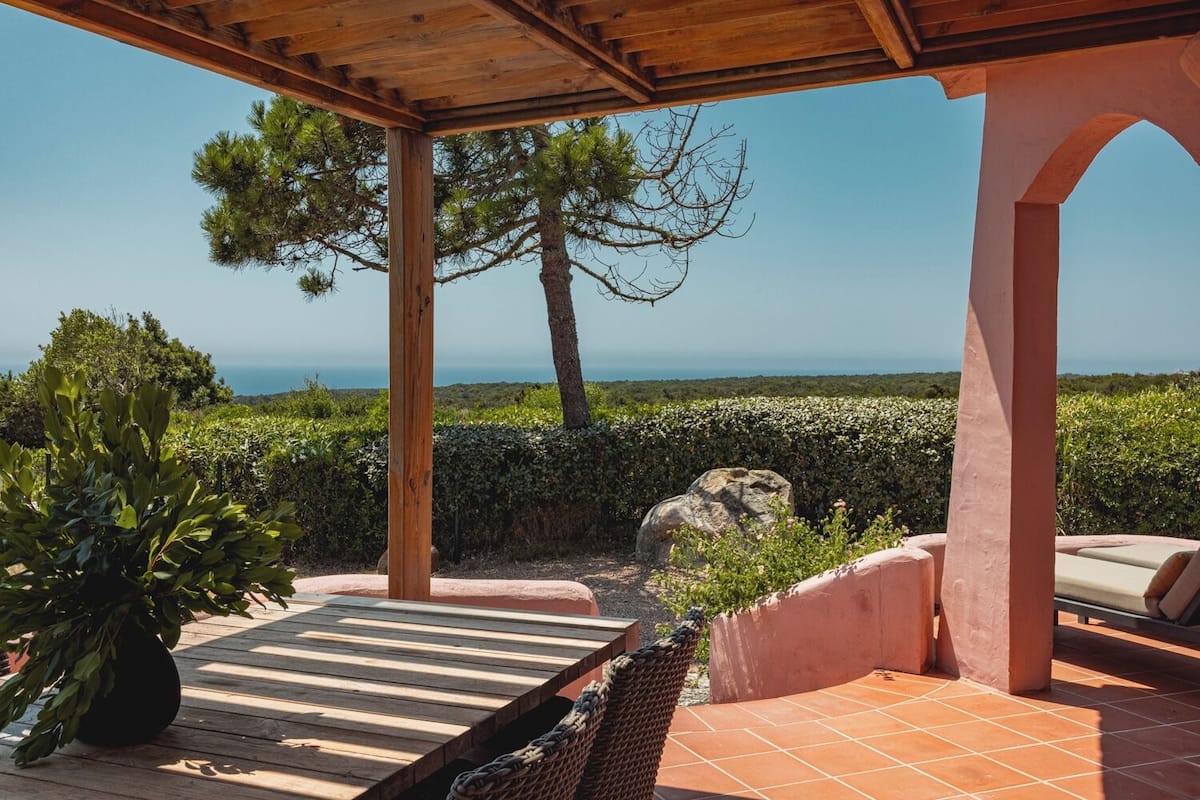 A covered outdoor seating area with a view of the sea, wooden pergola, and a potted plant.