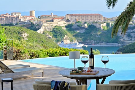 A poolside area with a table set for two, a bottle of wine, and a glass of red wine.