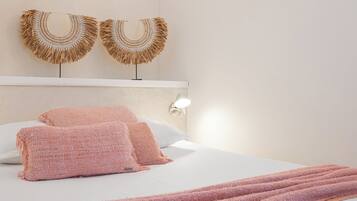 Una cama bien tendida con almohadillas rosadas con textura y una colcha, una lámpara de pared y dos obras de arte con flecos.