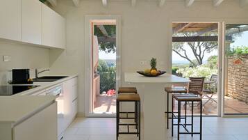 A modern kitchen with white cabinets, a central island with stools, and a view of the outdoors through a glass door.