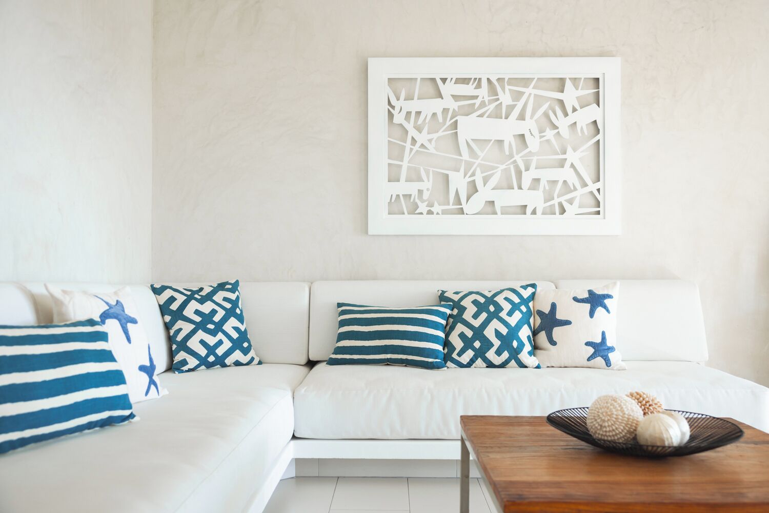 Un sofá blanco con cojines estampados, una obra de arte en la pared y una mesita con objetos decorativos.