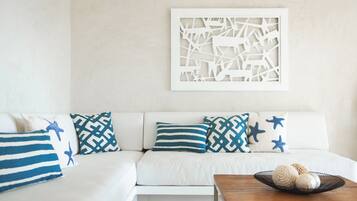Un sofá blanco con cojines estampados, una obra de arte en la pared y una mesita con objetos decorativos.