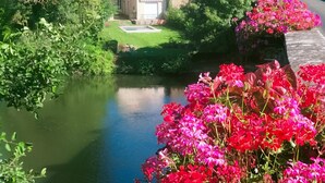 A serene riverside view with lush greenery and vibrant flowers. - Family Retreat: Heated Pool, Garden, Near Zoo & Le Mans Circuit (Bazouges-sur-le-Loir)