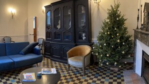 A living room with a checkered floor, a blue sofa, a wooden cabinet, a small Christmas tree, and a fireplace.