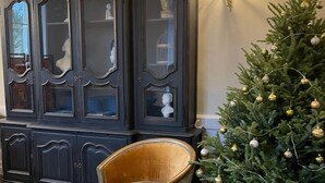 A room with a checkered floor, a dark wooden cabinet with glass doors, and a Christmas tree with ornaments.