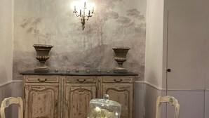 A dining area with a table set for two, a decorative wall with a tree mural, and a candelabra.