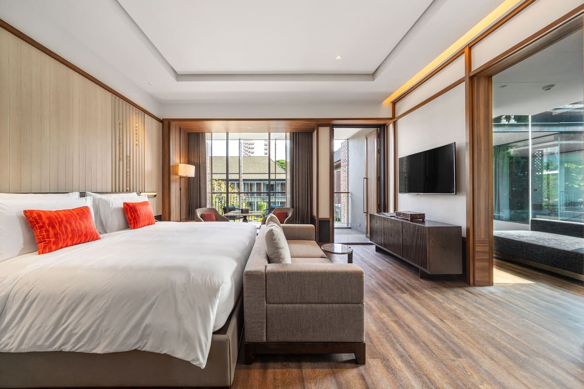 A modern hotel room with a large bed, a sofa, a TV, and a balcony with a view of the city.