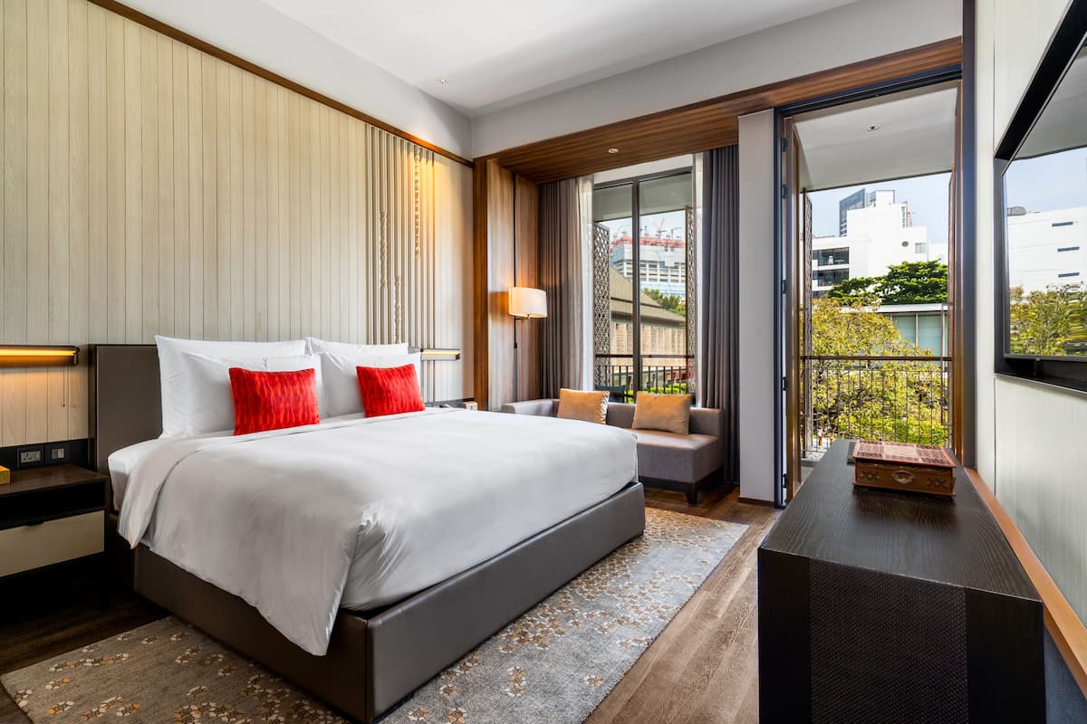 A modern hotel room with a large bed, a seating area, and a balcony with a city view.